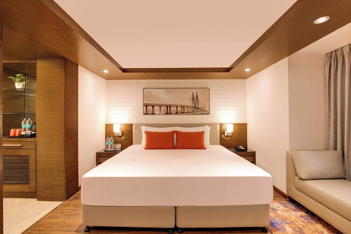 A hotel room with a large bed, two bedside tables, a sofa, a wall-mounted artwork, and a built-in shelf with toiletries.