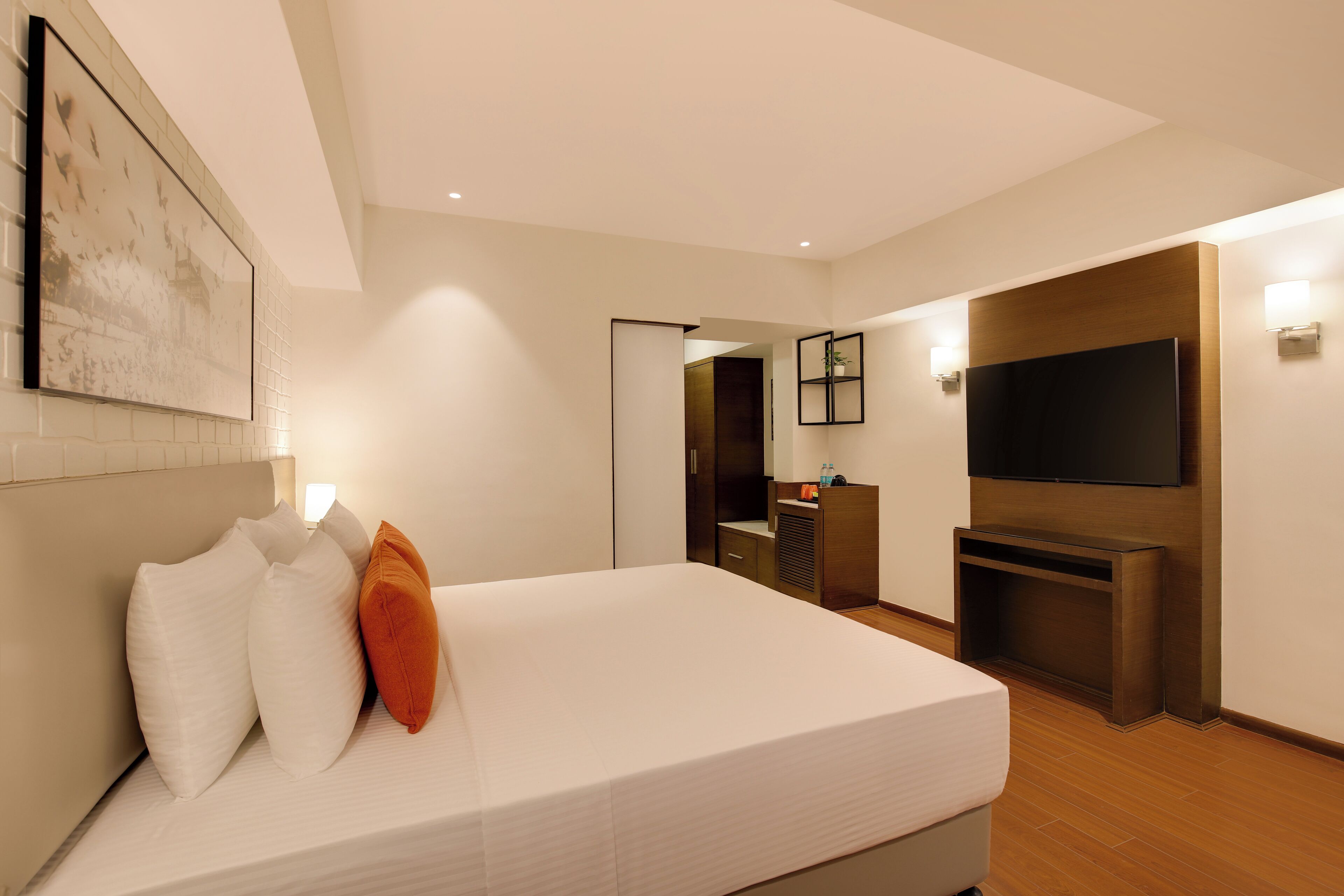 A modern hotel room with a large bed, a flat-screen TV mounted on the wall, a small desk, and a door leading to a bathroom.