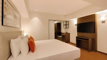 A modern hotel room with a large bed, a flat-screen TV mounted on the wall, a small desk, and a door leading to a bathroom.