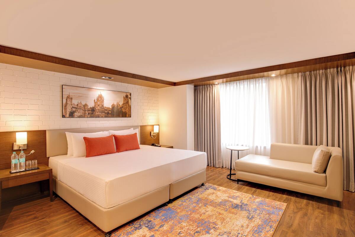 A hotel room with a large bed, a sofa, a small table, and a painting on the wall.