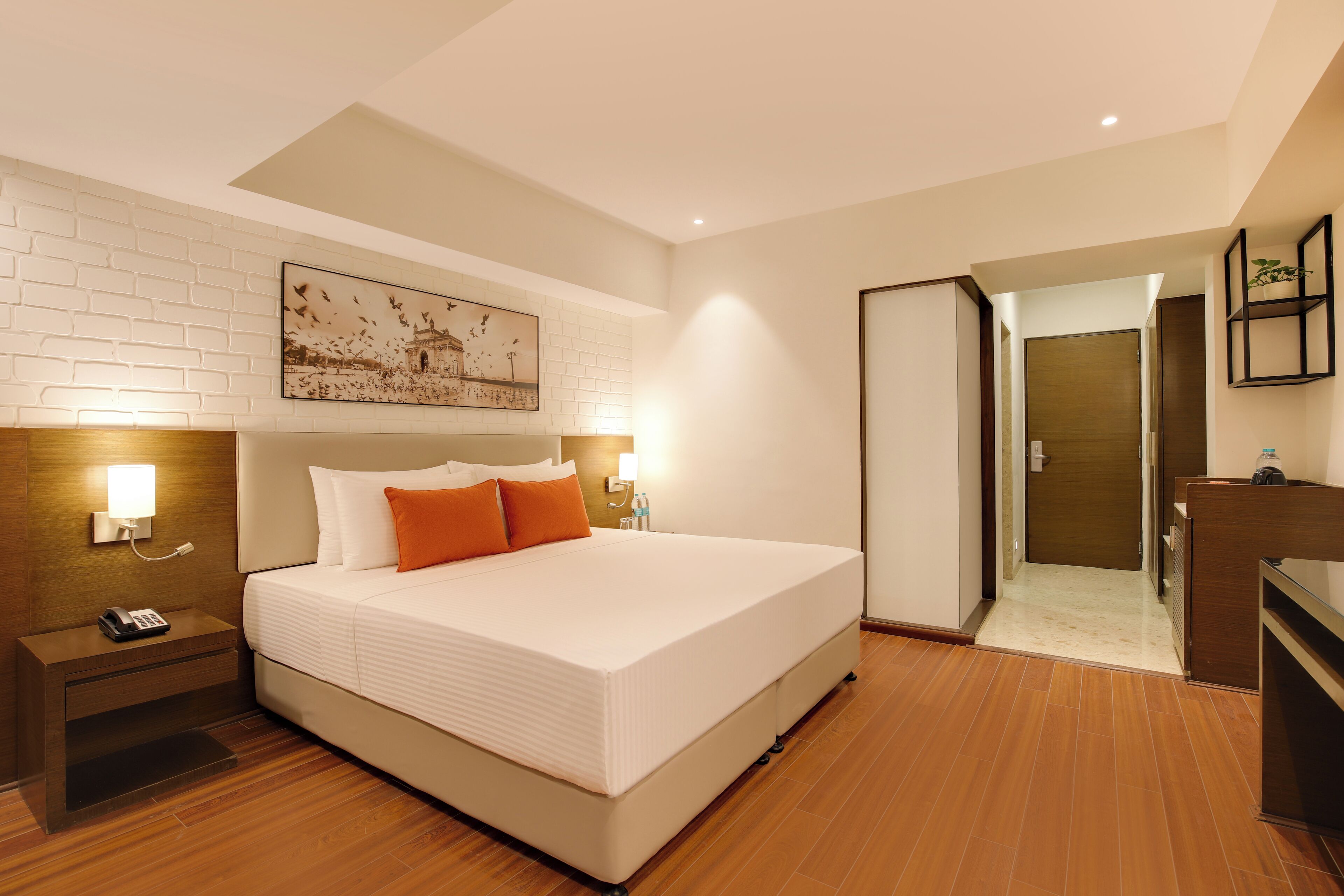 A hotel room with a large bed, a nightstand, a bedside lamp, a wall-mounted picture, and a door leading to a bathroom.