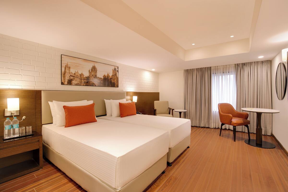 A hotel room with a large bed, two bedside tables, a chair, a small table, and a painting on the wall.