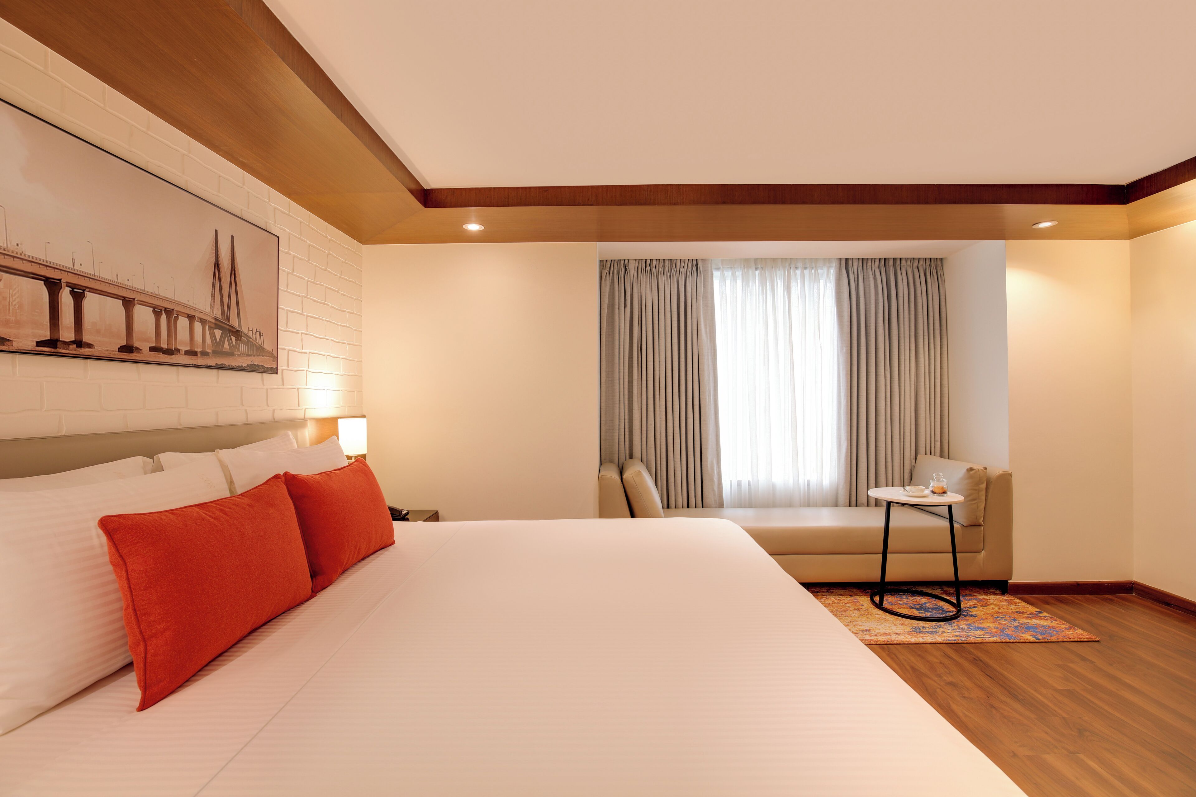 Een hotelkamer met een groot bed, een klein tafeltje, een bank en een raam met gordijnen.