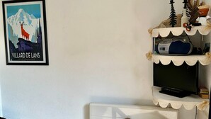 A room with a framed picture on the wall, a television on a shelf, and a wooden chair.