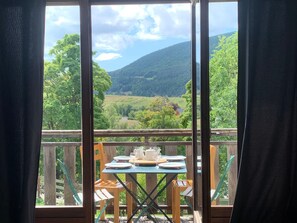 A balcony with a table set for dining, overlooking a scenic landscape with trees and hills.