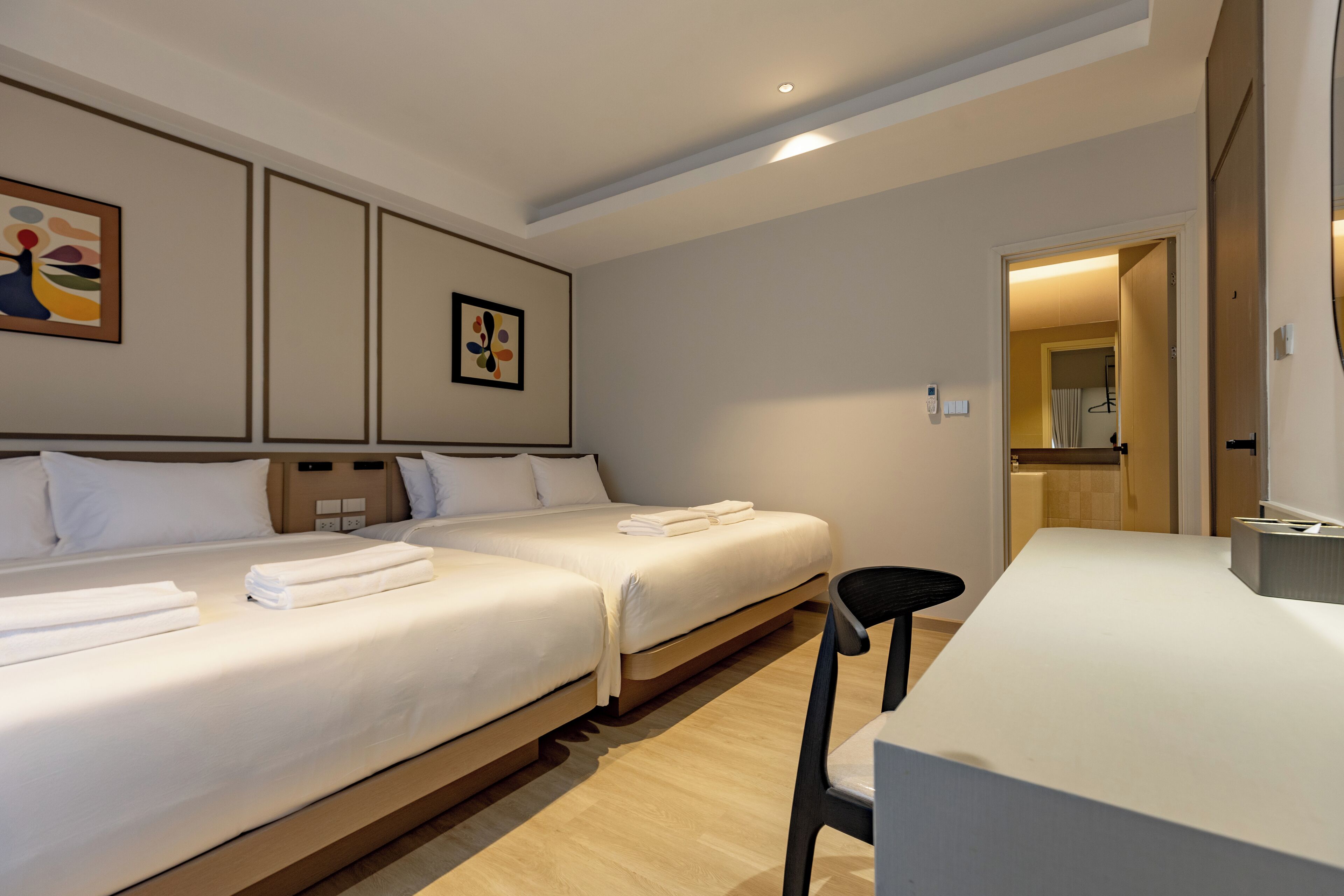 Een hotelkamer met twee bedden, een bureau en een stoel. Er hangen afbeeldingen in lijsten aan de muur.