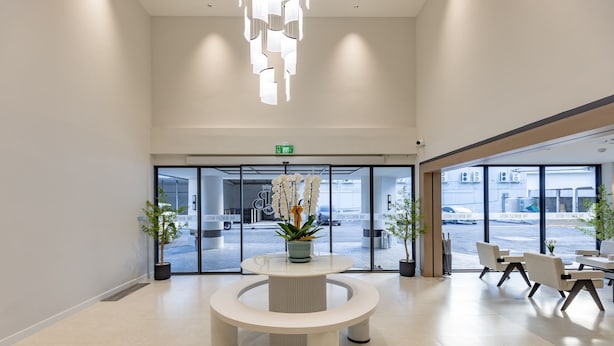 Een moderne hotellobby met een ronde centrale tafel, potplanten en een zithoek.