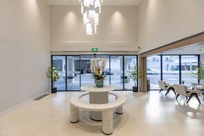 A modern hotel lobby with a central round table, potted plants, and seating area. -  The Bentley Hotel Pratunam (Bangkok)