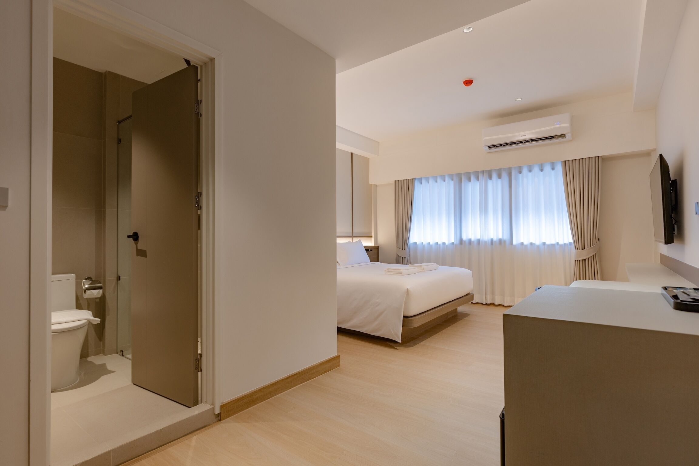 A modern hotel room with a shower, a bed, a desk, and a TV.