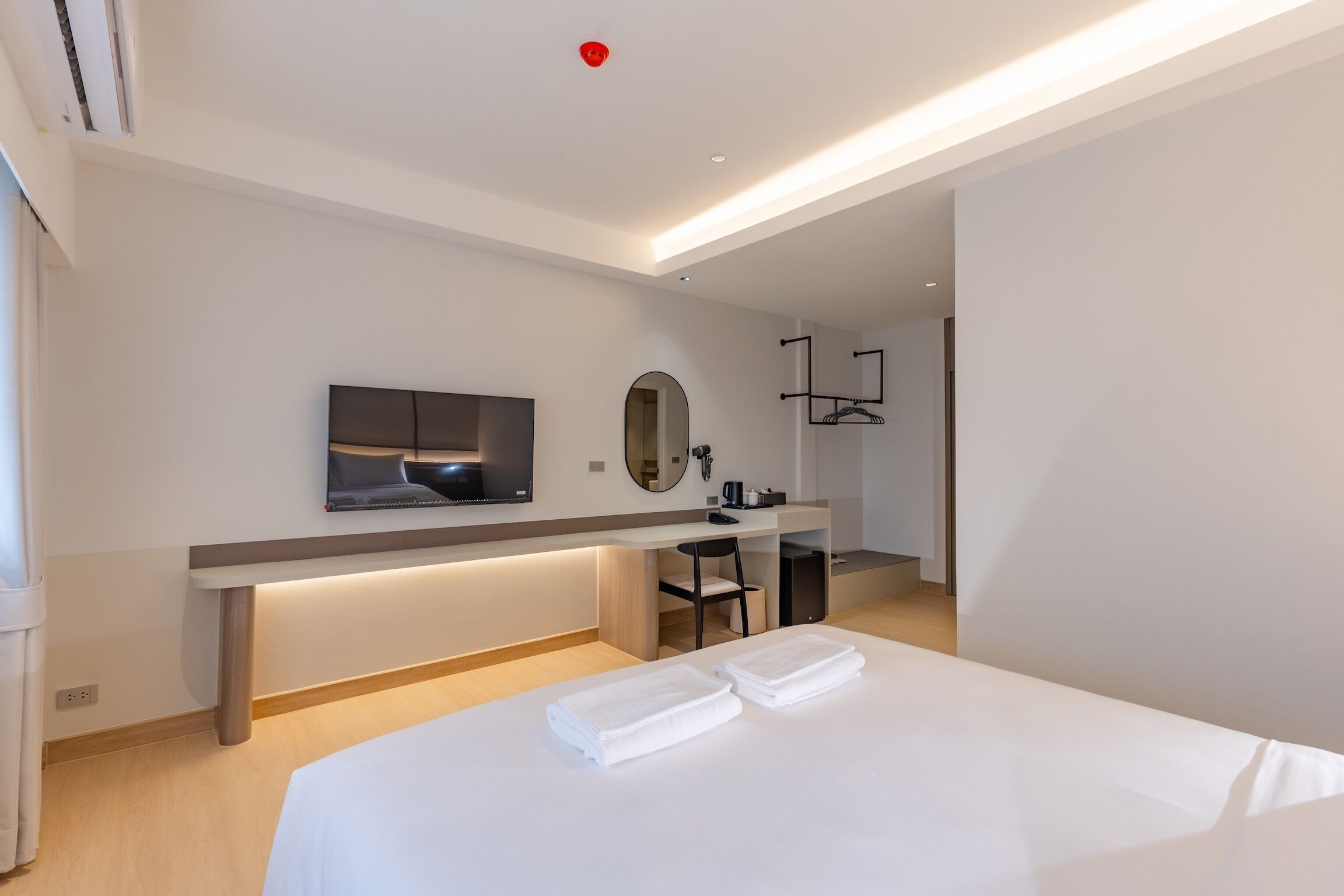 Ein modernes Hotelzimmer mit Bett, Schreibtisch, Stuhl, Fernseher und Spiegel.