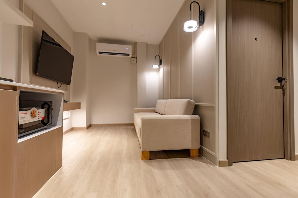 Une chambre d’hôtel moderne équipée d’un téléviseur à écran plat fixé au mur, d’un four à micro-ondes encastré, d’un canapé et d’une porte en bois.