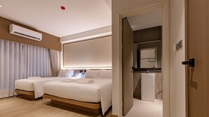 Een moderne hotelkamer met twee bedden, een groot raam, een airconditioning en een badkamer die door een open deur zichtbaar is.
