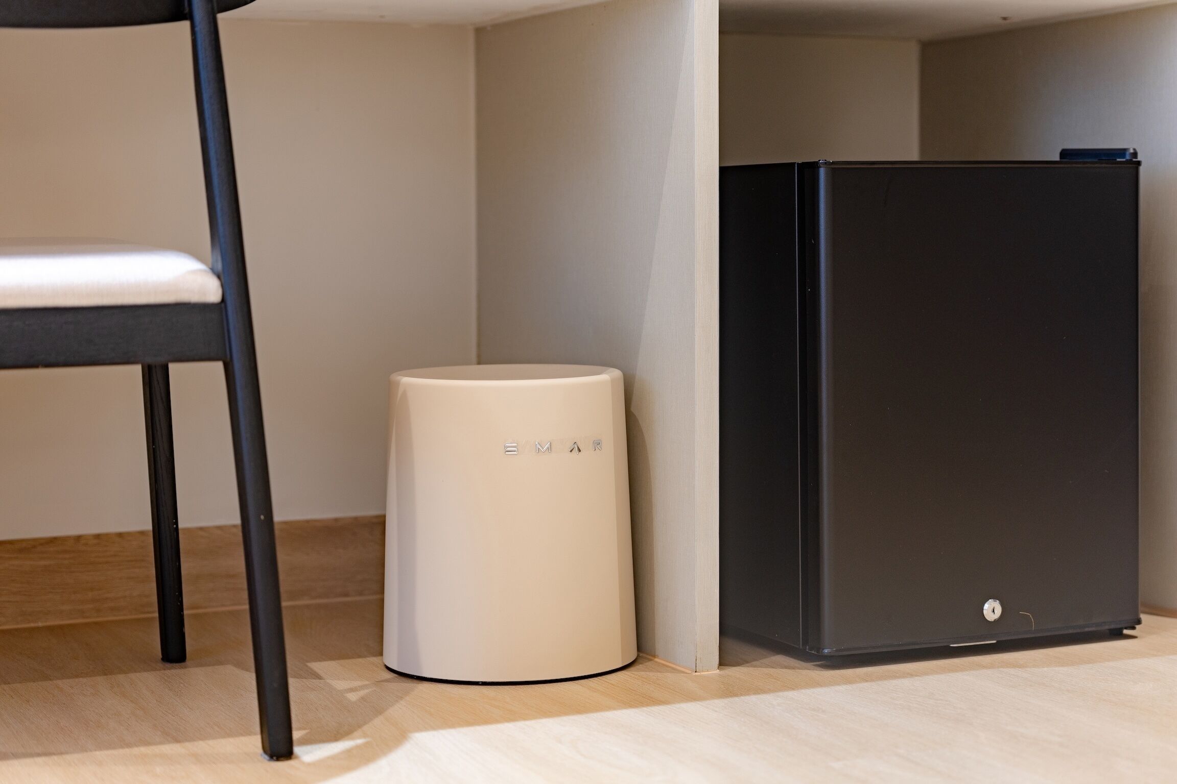 A compact, modern room with a minimalist design, featuring a black cabinet, a white cylindrical object, and a black chair.