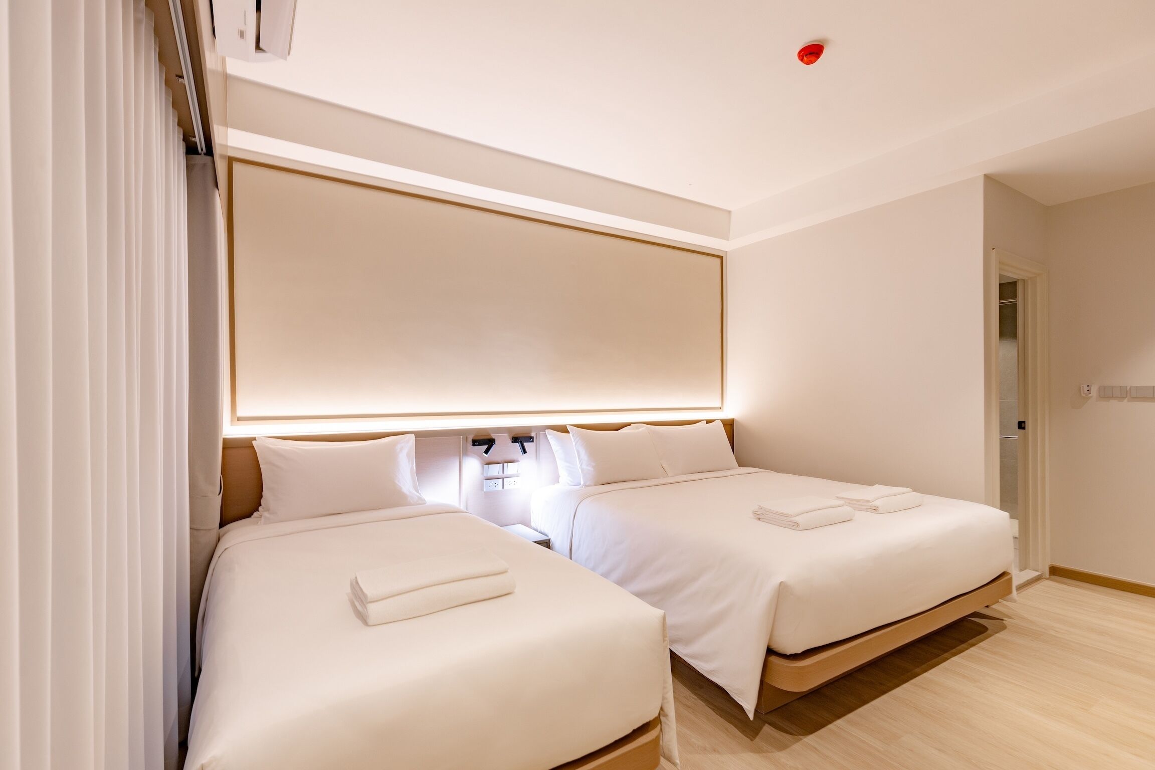 A hotel room with two beds, a large mirror above the beds, and a red ceiling light.