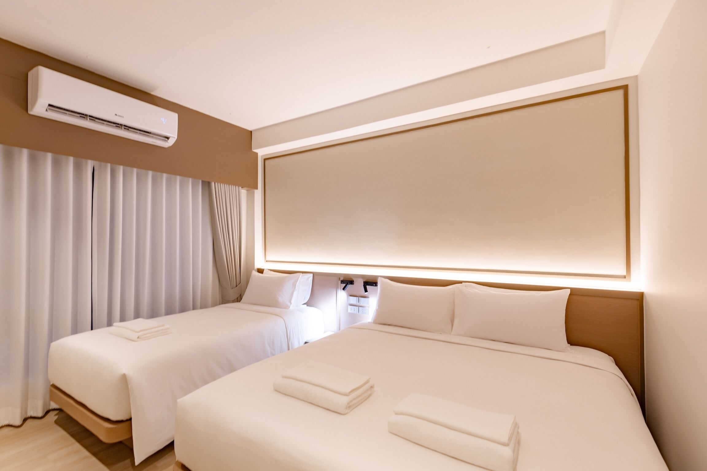 Habitación de hotel con dos camas, un televisor grande montado en la pared y un equipo de aire acondicionado.