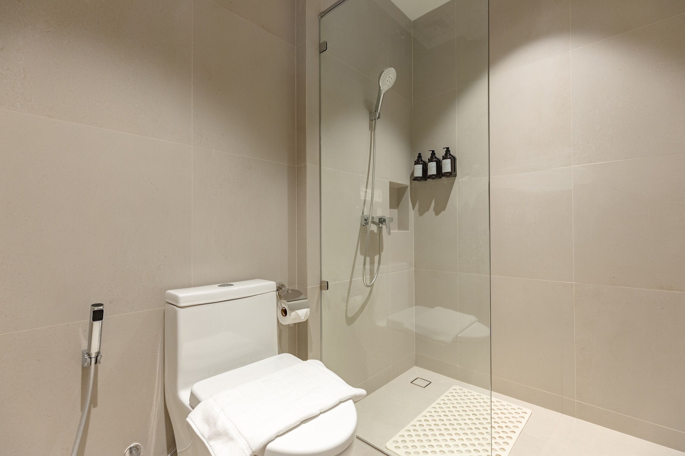 A modern bathroom with a glass-enclosed shower, a toilet, and a shelf with toiletries.