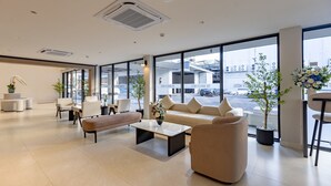 Een ruime lobby met een bank, stoelen, een salontafel en potplanten.