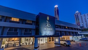 Een hotel ingang met een groot bord, een parkeerplaats en een hoog gebouw op de achtergrond.