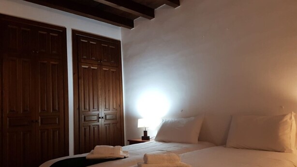 Um quarto com uma cama, duas almofadas brancas, uma mesa de cabeceira e um guarda-roupa de madeira.
