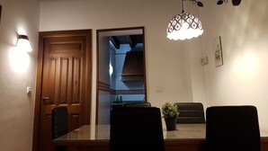 Uma sala de jantar com uma mesa de madeira, duas cadeiras, uma planta em vaso e um lustre.