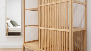 A wooden shelving unit with multiple compartments, a bed with a green pillow, and a window in the background.
