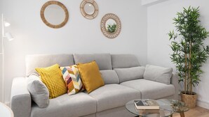A modern living room with a grey sofa, colorful cushions, a glass coffee table, and decorative wall mirrors.