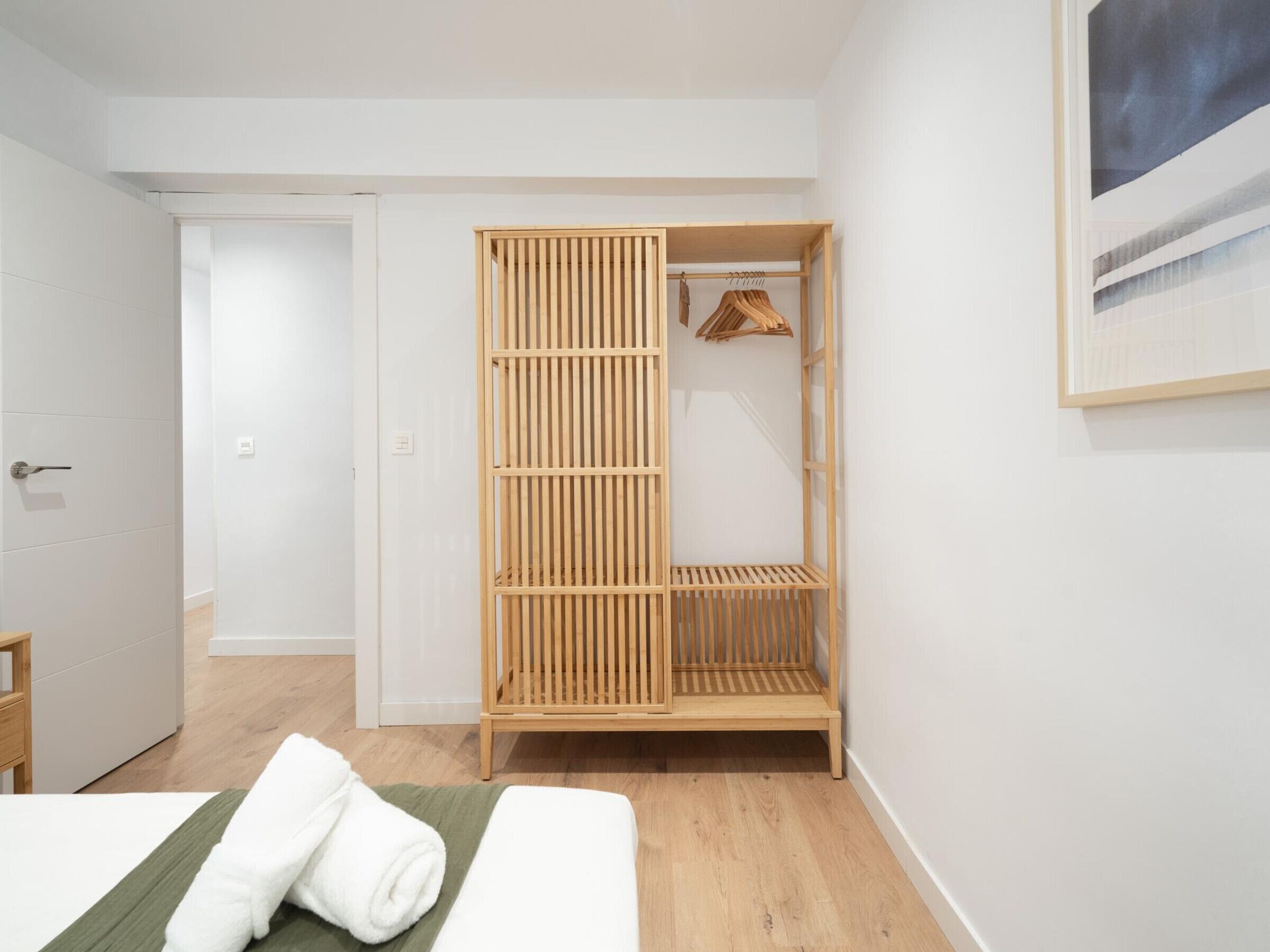 A bedroom with a wooden wardrobe, a bed with a green bedspread, and a white towel.