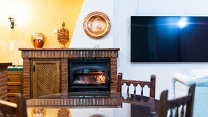 A living room with a brick fireplace, a round table, and a flat-screen TV mounted on the wall. - Charming House in Albaicín, Granada (Granada)