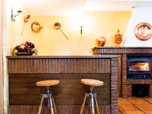 A kitchen with two stools, a brick fireplace, and a fruit bowl on the counter.