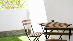 Un conjunto de mesa y silla de madera pequeña en un espacio exterior soleado, con piso de césped artificial verde y una pared blanca.