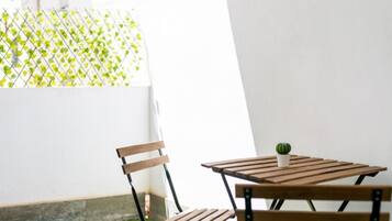 Een klein houten tafeltje met stoelen in een zonnig buitengebied, met een vloer van kunstgras en een witte muur.