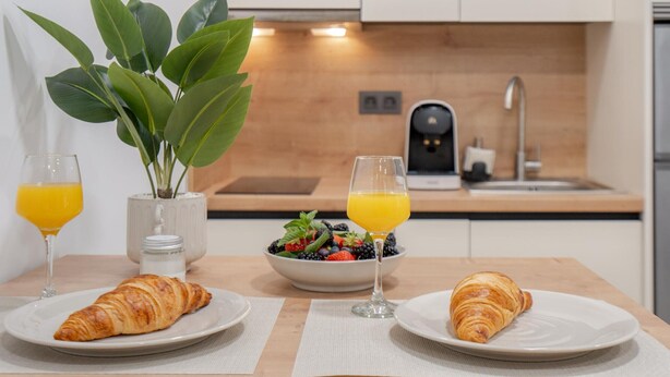 A breakfast setup with croissants, a bowl of mixed berries, and glasses of orange juice on a wooden table in a modern kitchen.