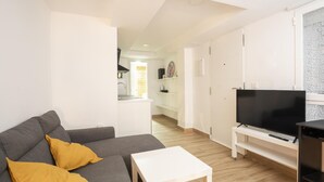 Een moderne woonkamer met een grijze bank, een witte salontafel en een flatscreen televisie op een standaard.