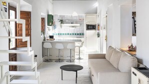 A modern kitchen with white cabinets, a central island, and bar stools. There is a white sofa and a small table in the living area. - Apartment in Granada with private pool and air conditioning (Granada)
