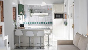 A modern kitchen with a central island, white bar stools, and a dining area with a sofa. - Apartment in Granada with private pool and air conditioning (Granada)
