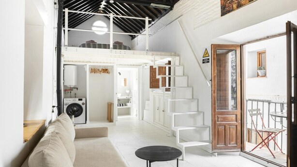 A spacious loft with a high ceiling, a staircase leading to an upper level, a sofa, a small table, and a view of the outside. - Apartment in Granada with private pool and air conditioning (Granada)