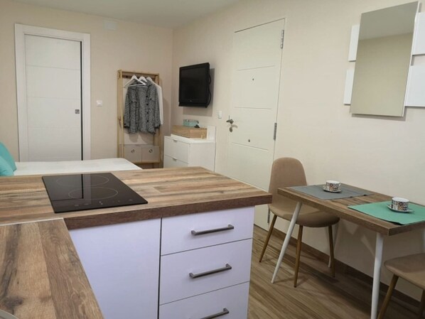 Una habitación compacta con kitchenette, comedor y cama.