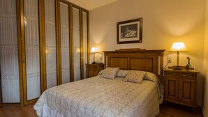 A neatly arranged bedroom with a large bed, wooden headboard, two bedside tables with lamps, and a wardrobe with curtains. - Charming Apartment in Historical Center Near Granada Cathedral (Granada)