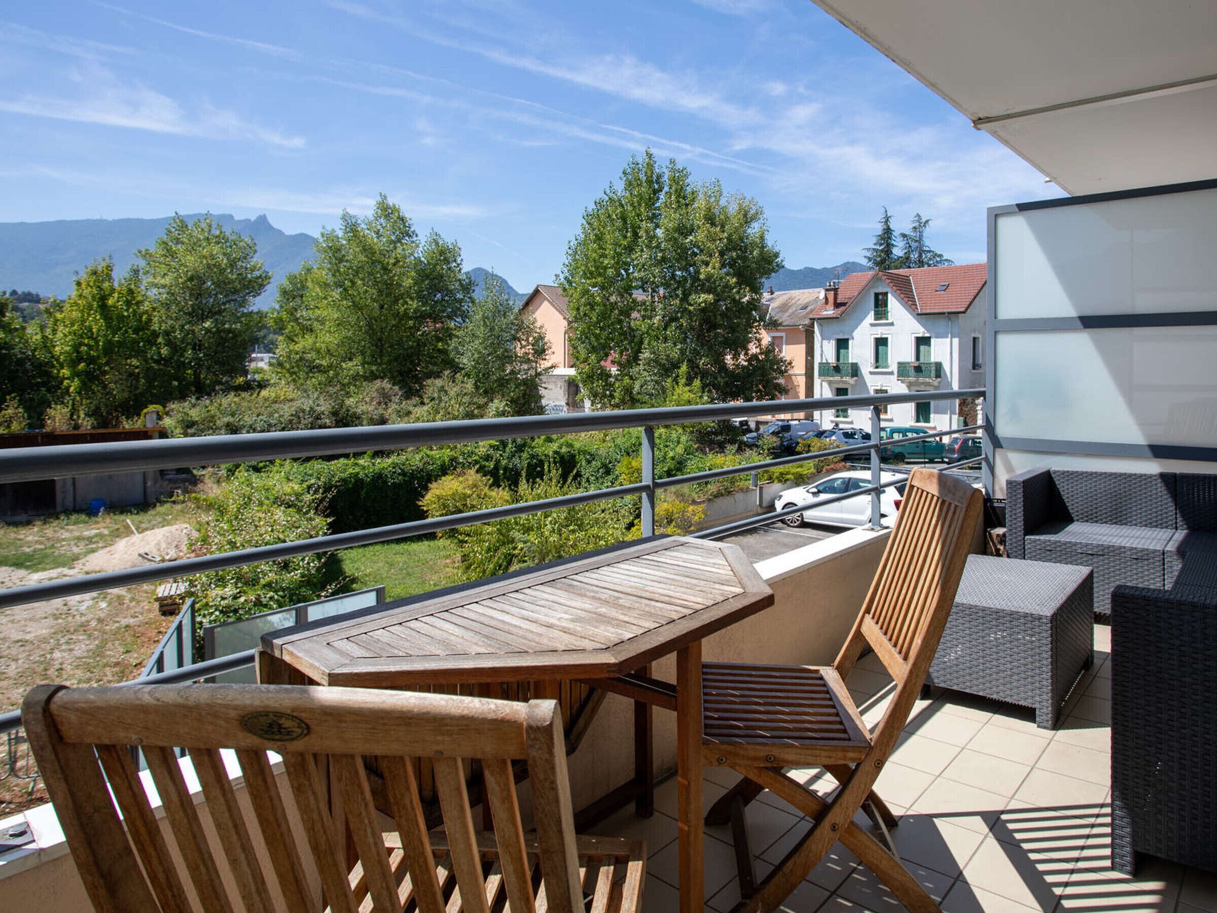 A balcony with a wooden table and chairs, overlooking a residential area with houses and trees.
