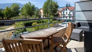 Un balcon doté d’une table et de chaises en bois, donnant sur un quartier résidentiel avec des maisons et des arbres.