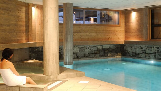 Un espace de bien-être avec une piscine, des murs en pierre et des colonnes en bois.