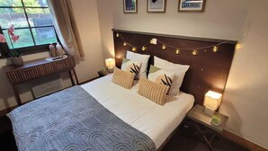 Un lit bien fait, recouvert d’une couverture à motifs, une table de chevet avec une lampe et des œuvres d’art accrochées au mur au-dessus du lit.