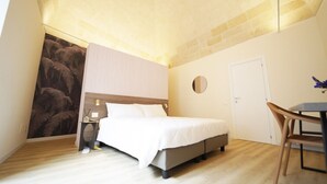 A bedroom with a bed, a bedside table, a mirror, a door, and a small table with a chair. - La Chicca - Large Suite - Matera (Matera)