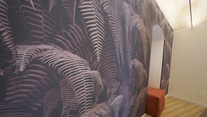 A room with a large fern leaf pattern wallpaper, a wooden floor, and a white wall. - La Chicca - Large Suite - Matera (Matera)