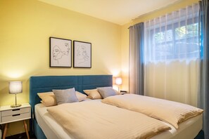 A double bed with a blue headboard, two bedside tables with lamps, and two framed artworks on the wall.