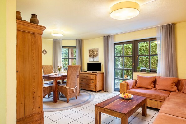 A living room with a sofa, a dining table with chairs, a TV, and a cabinet.