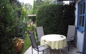 A patio with a round table and two chairs, surrounded by greenery and a potted plant.