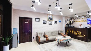 Zona de recepción de un hotel con mostrador de recepción, un sofá, una mesita con mantel colorido y varias lámparas colgantes.