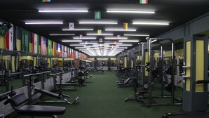 Un gimnasio con equipo de levantamiento de pesas, espejos y banderas de distintos países.