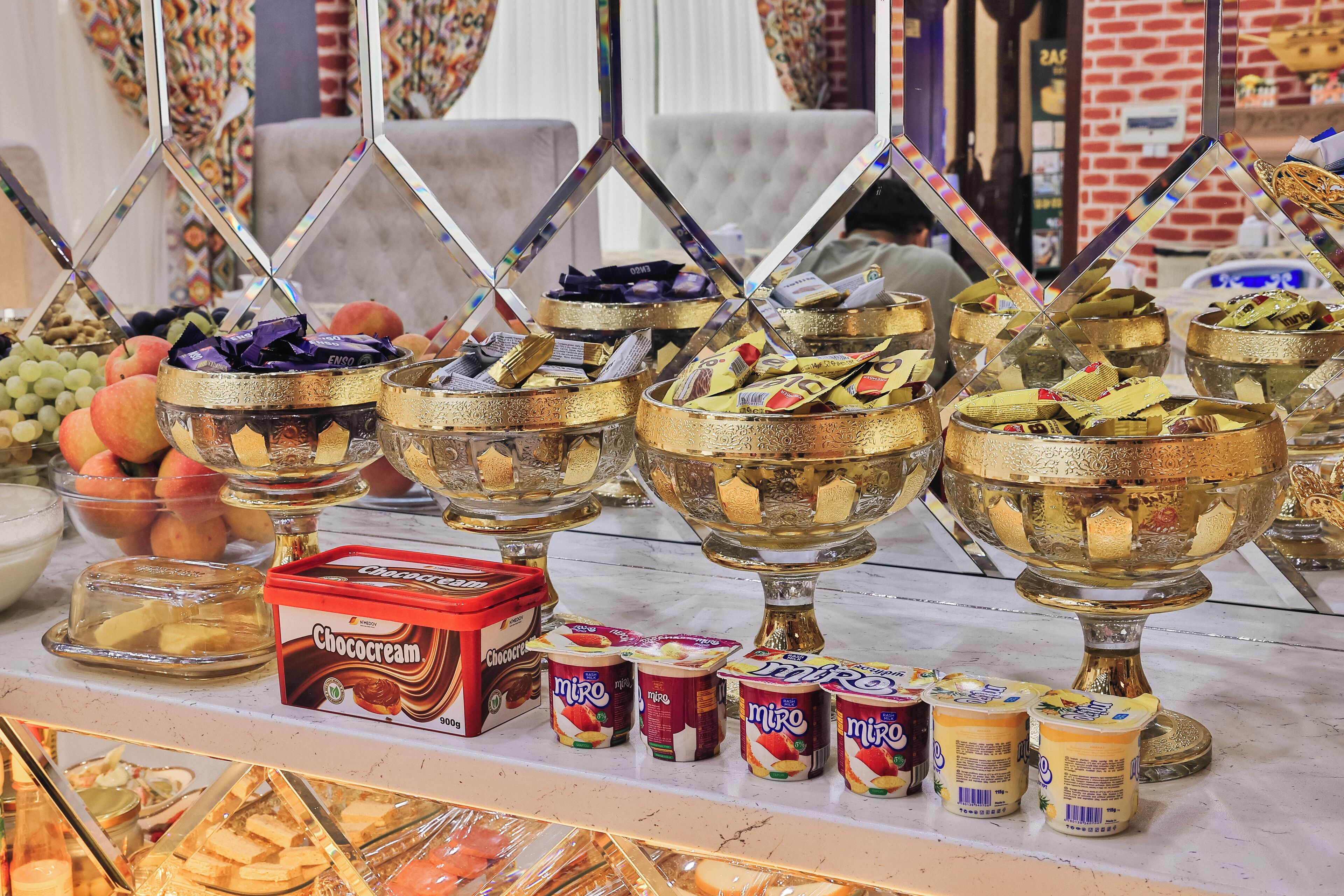A buffet with various food items including fruits, chocolates, and yogurt.